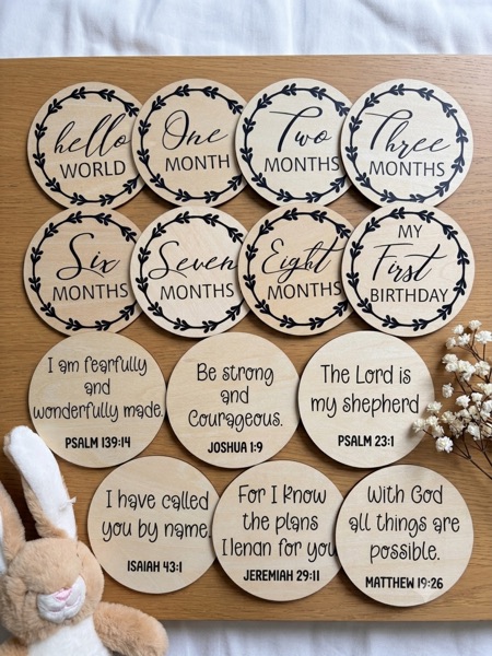 Natural wooden milestone discs reading Hello World, One Month through Eight Months and My First Birthday, with Bible verse discs such as The Lord is my shepherd, Psalm 23:1.
