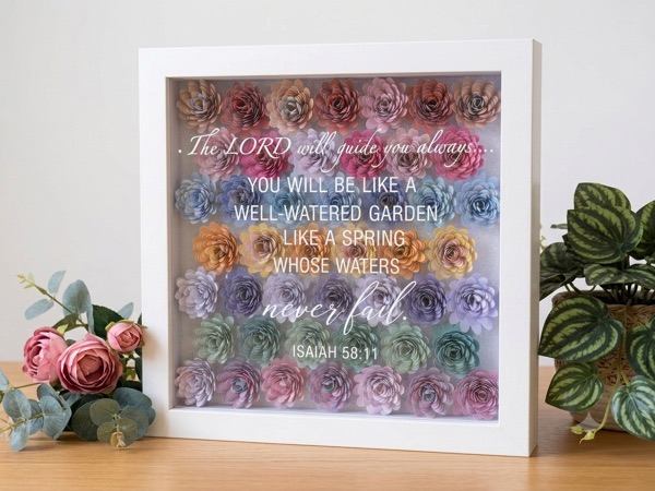 Shadow box filled with rows of rainbow-coloured paper flowers, lettered with Isaiah 58:11: You will be like a well-watered garden.
